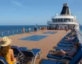 Pasajeros disfrutando la cubierta de un crucero durante el d�a, con vista al mar y clima perfecto para relajarse.